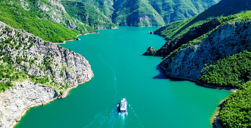 Boat cruising through Komani Lake surrounded by lush mountains in Albania.
