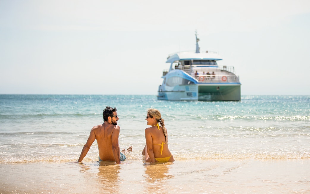 Couple sitting on Moreton Island beach with a boat in the background.