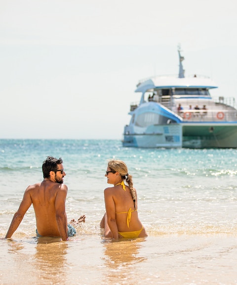 Couple sitting on Moreton Island beach with a boat in the background.