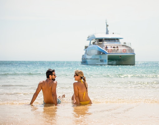 Couple sitting on Moreton Island beach with a boat in the background.