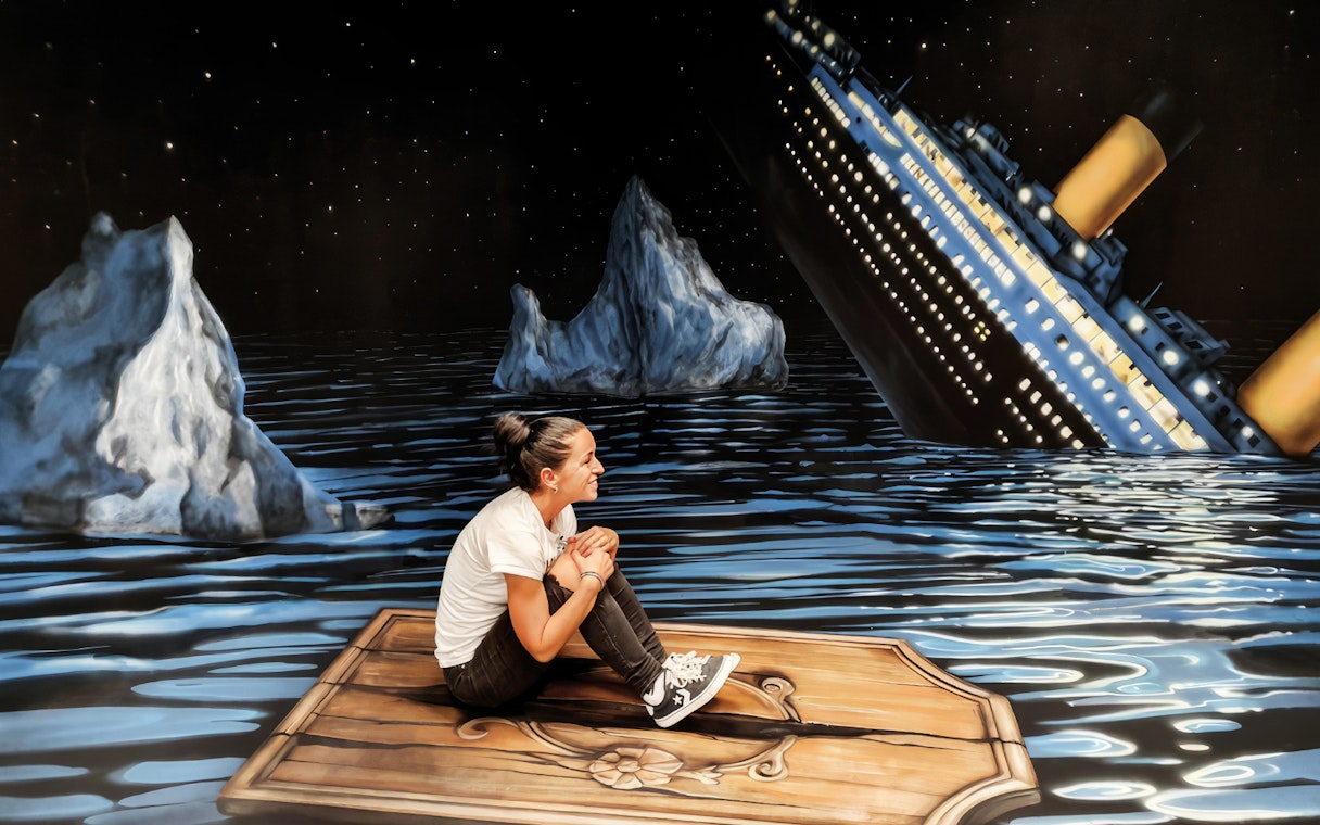 Person sitting on a wooden plank in front of a sinking ship illusion at the Museum of Fantastic Illusions.