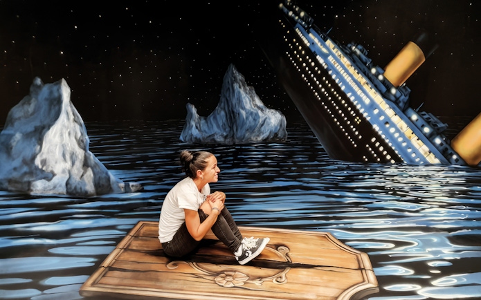 Person sitting on a wooden plank in front of a sinking ship illusion at the Museum of Fantastic Illusions.