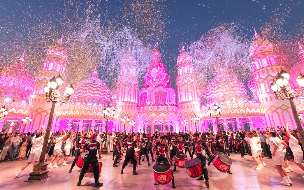 Drummers performing at Global Village Dubai with vibrant pink-lit architecture.