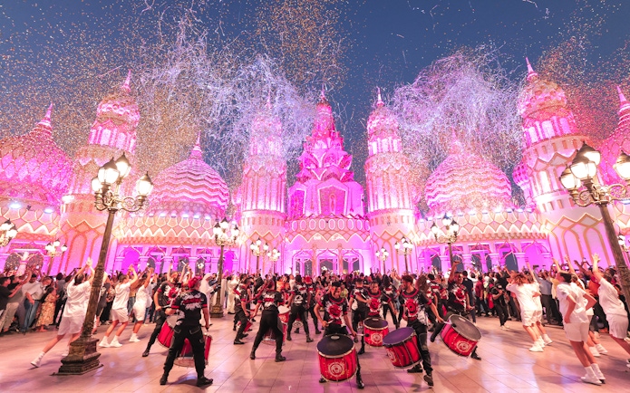 Drummers performing at Global Village Dubai with vibrant pink-lit architecture.