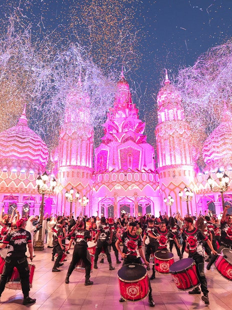 Drummers performing at Global Village Dubai with vibrant pink-lit architecture.