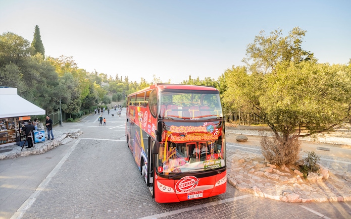 Athens city tour hop-on hop-off bus near a park with people walking.