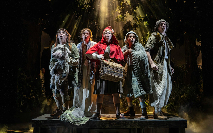 Characters in a forest scene from "Into the Woods" musical, holding a basket and a puppet cow.