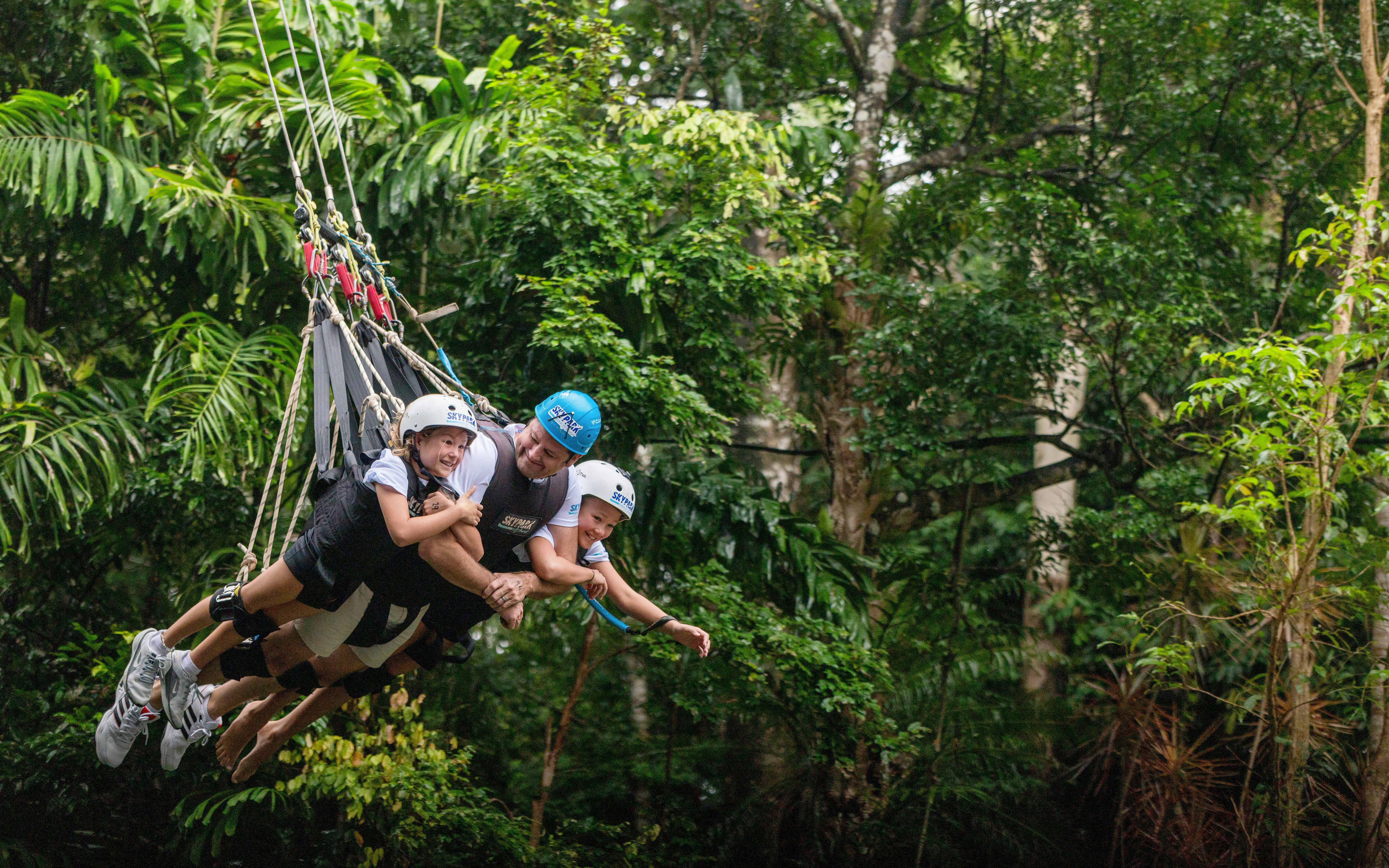 Visitors enjoying a group triple swing at Skypark Cairns amidst lush greenery.