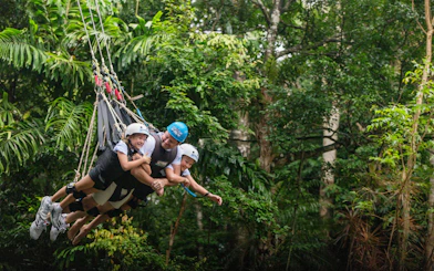 Visitors enjoying a group triple swing at Skypark Cairns amidst lush greenery.