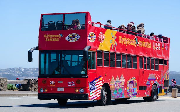 Red double-decker sightseeing bus in San Francisco with tourists on top deck.