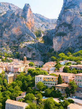 Village nestled between cliffs in Gorges du Verdon, France, with colorful houses and lush greenery.