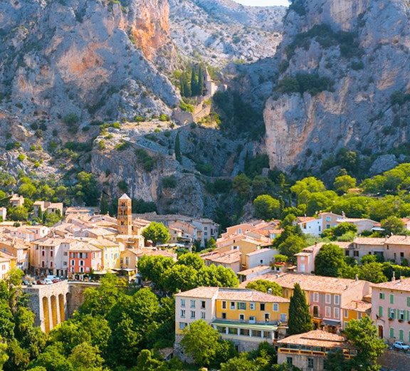 Village nestled between cliffs in Gorges du Verdon, France, with colorful houses and lush greenery.