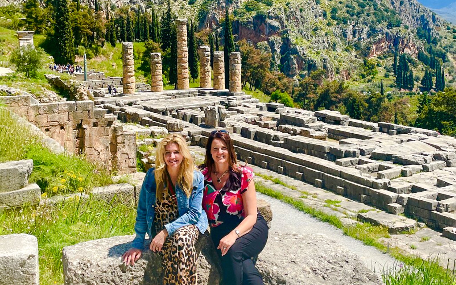 Visitors at Delphi Archaeological Site with ancient ruins and mountainous backdrop.