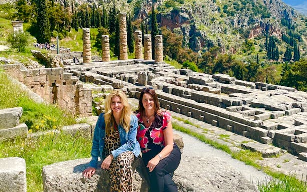 Visitors at Delphi Archaeological Site with ancient ruins and mountainous backdrop.