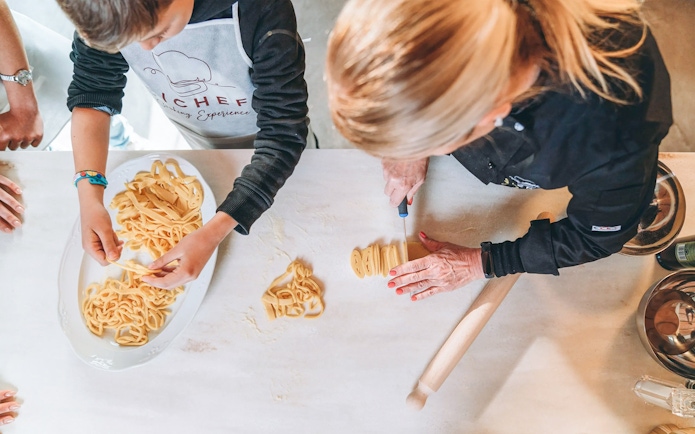 Making fresh pasta in a cooking class with a chef and participant.