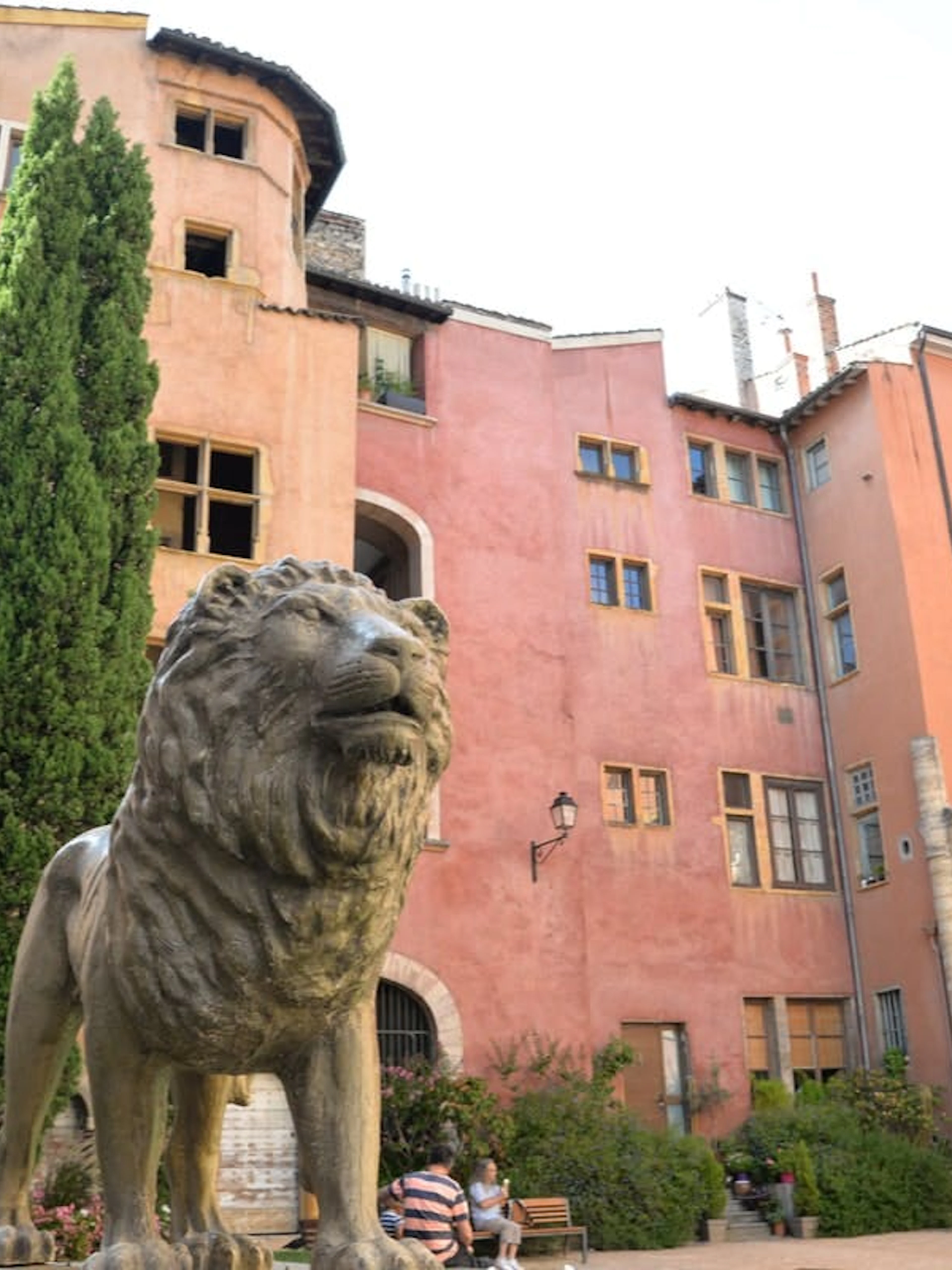 Lion statue in Lyon Old Town courtyard with historic pink buildings.