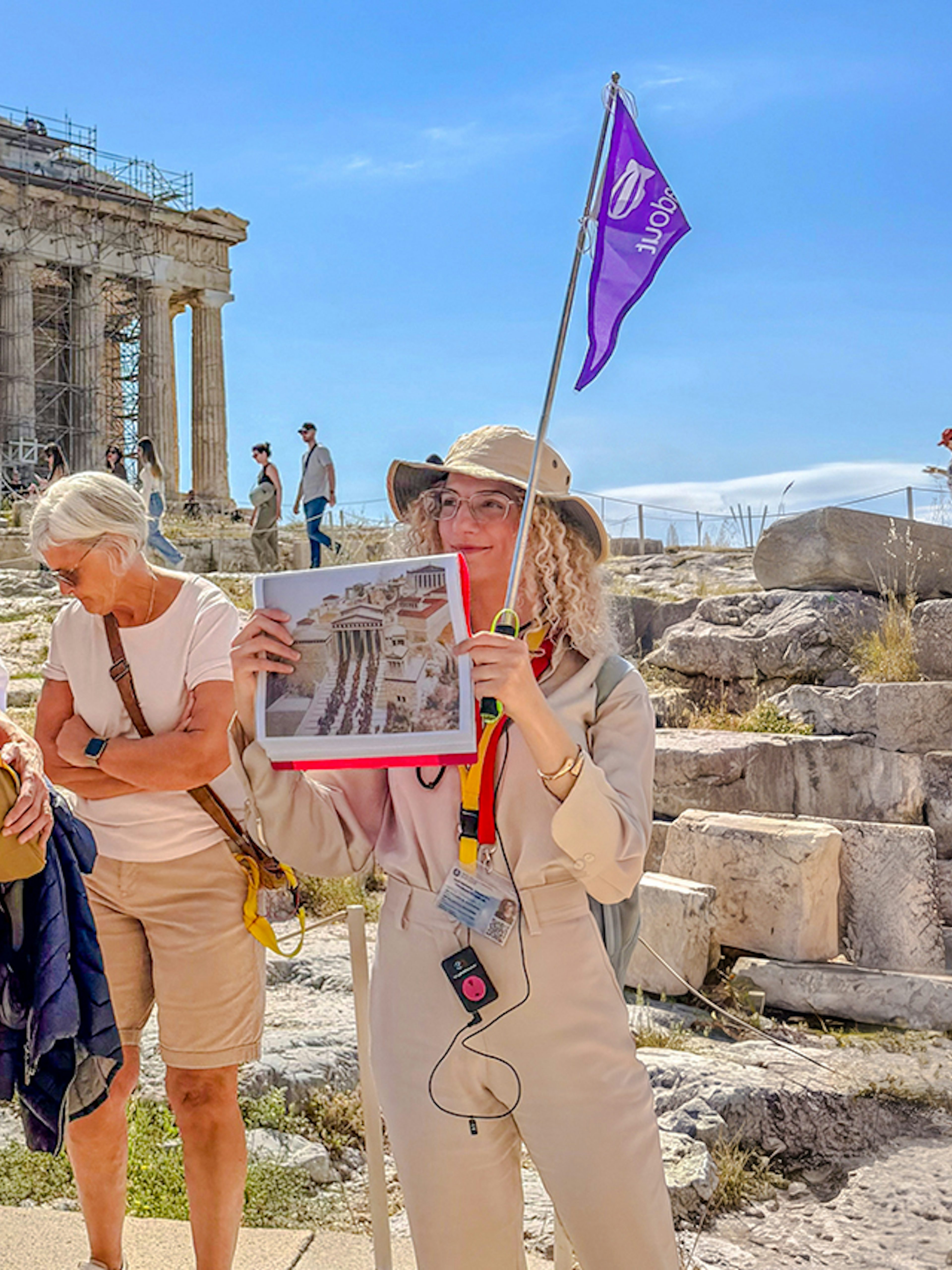 Guided tour group at the Acropolis in Athens with a guide holding a flag and image.