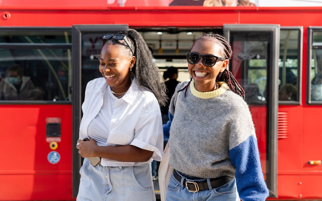 Women smiling as they exit a red hop-on hop-off bus.