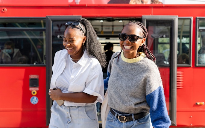 Women smiling as they exit a red hop-on hop-off bus.