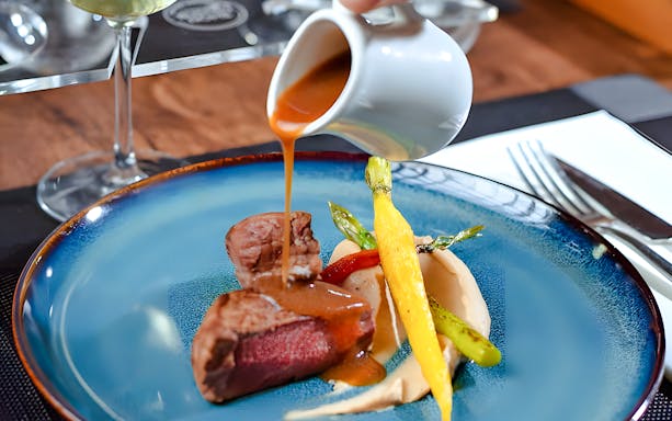Waiter pouring sauce over steak dish inside Bustronome Paris.