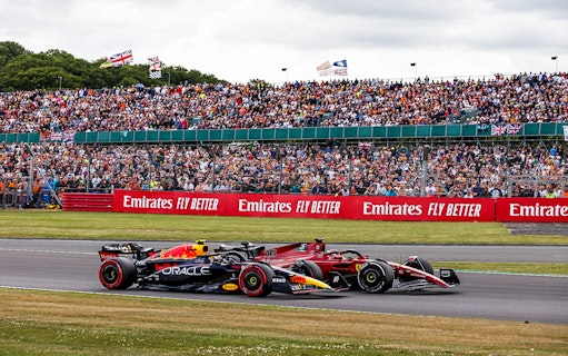 Two Formula 1 cars racing at the British Grand Prix, Silverstone, with a large crowd in the background.