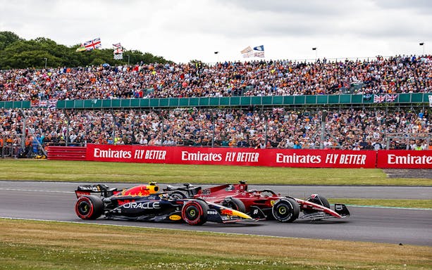 Two Formula 1 cars racing at the British Grand Prix, Silverstone, with a large crowd in the background.