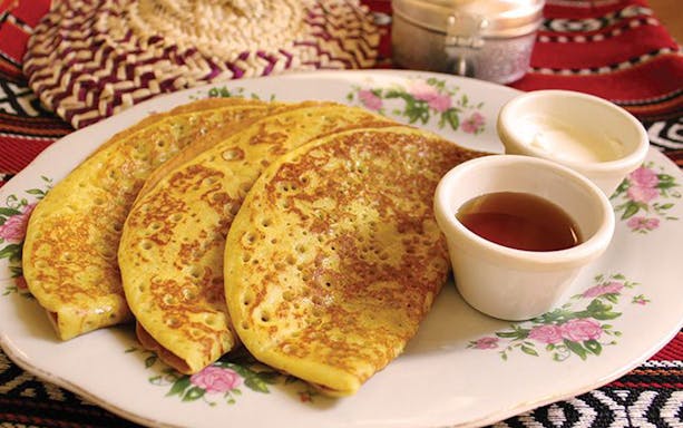 Emirati pancakes with honey and cream served on a floral plate during Burj Khalifa Sunset Abra Tour.