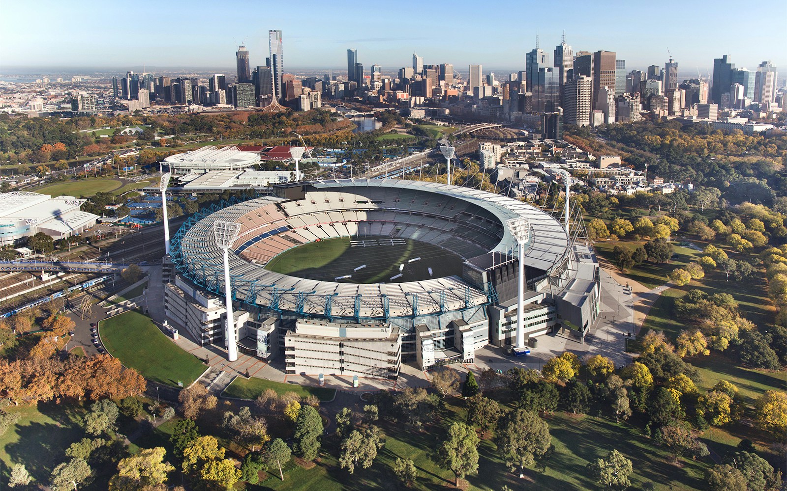 Aerial view of Melbourne Cricket Ground with city skyline in the background.