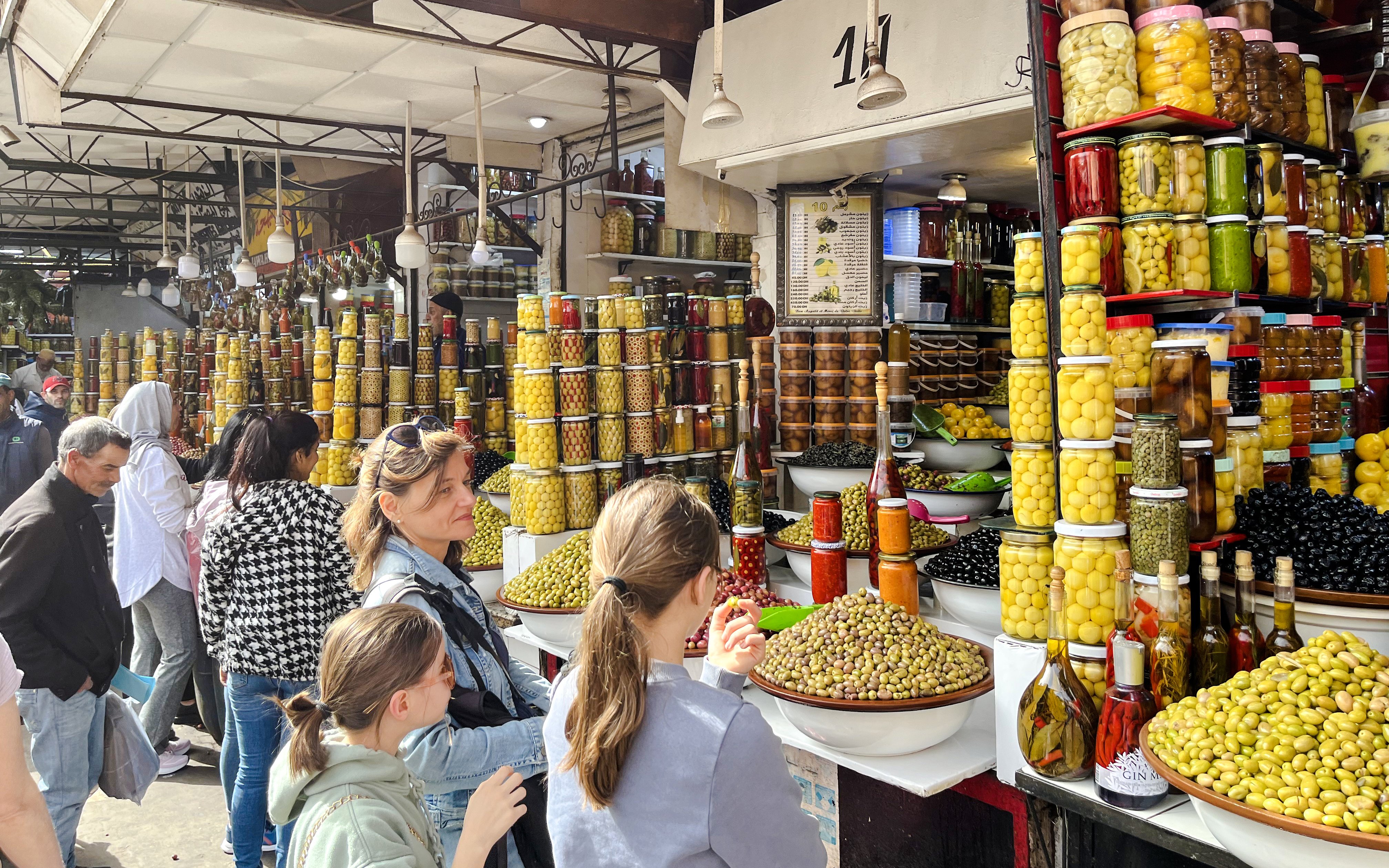 Visitors exploring olive and preserved goods stall in Marrakech Souks.