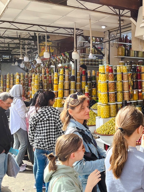 Visitors exploring olive and preserved goods stall in Marrakech Souks.