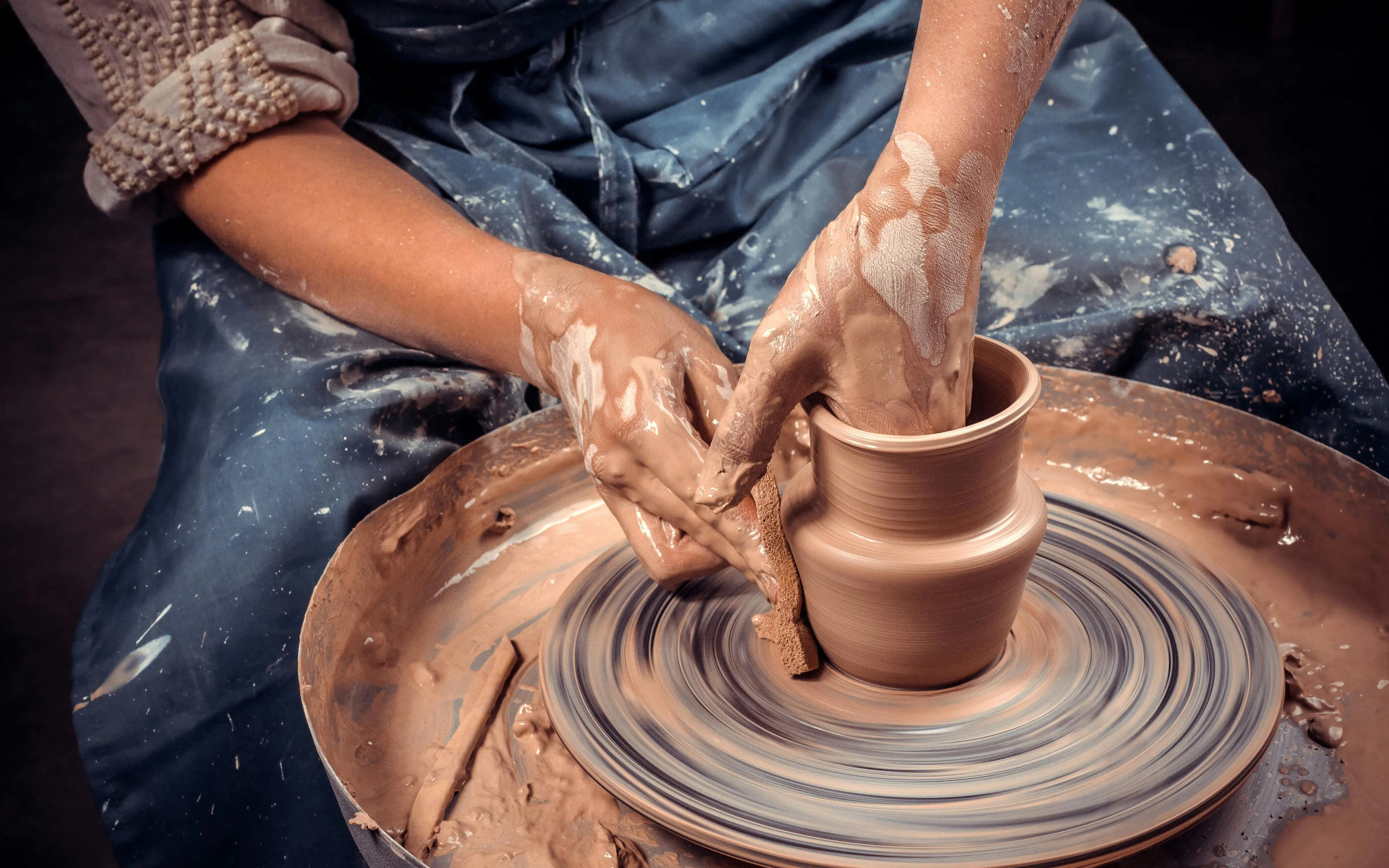 Craftsman shaping clay pot on pottery wheel, close-up of hands.