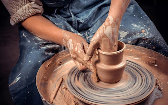 Craftsman shaping clay pot on pottery wheel, close-up of hands.