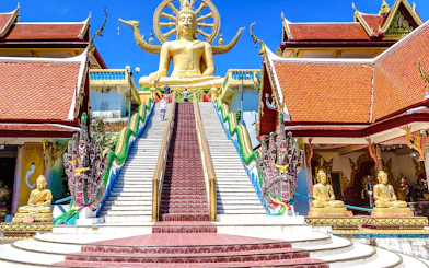 Big Buddha statue at Wat Phra Yai Temple, Koh Samui, with ornate staircase and dragon sculptures.