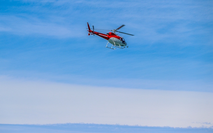 Helicopter flying over Kaikoura, New Zealand against a clear blue sky.
