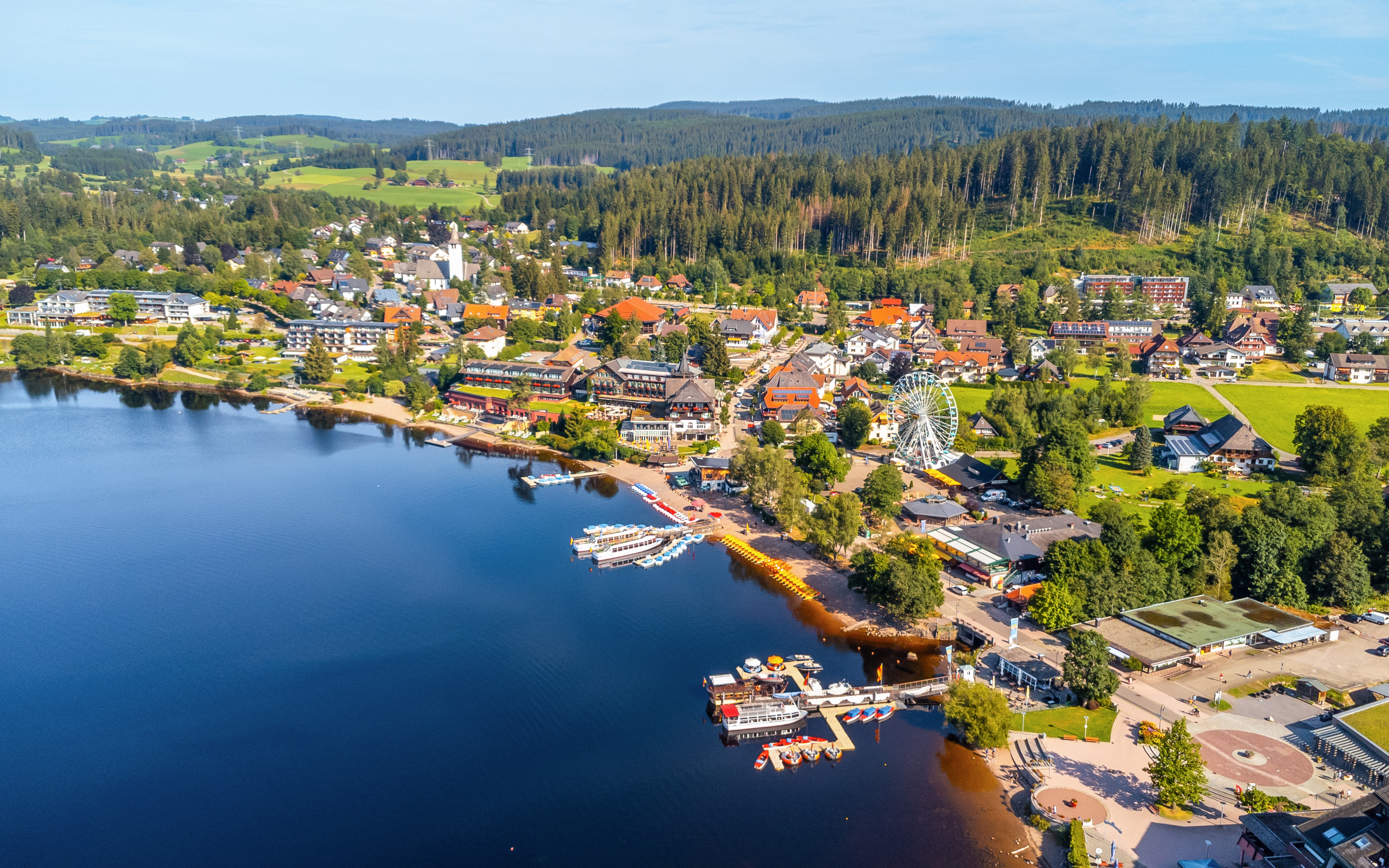 Aerial view of Lake Titisee with boats, a Ferris wheel, and surrounding village in Germany.