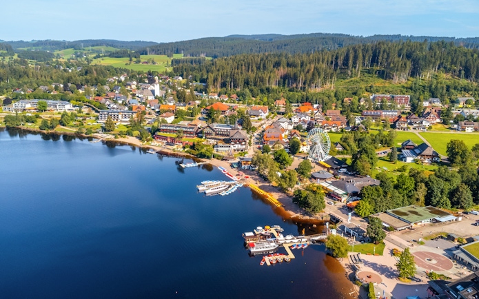 Aerial view of Lake Titisee with boats, a Ferris wheel, and surrounding village in Germany.
