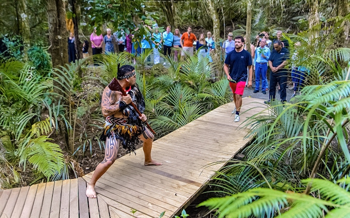 Warrior performing traditional challenge on forest path with tourists observing.