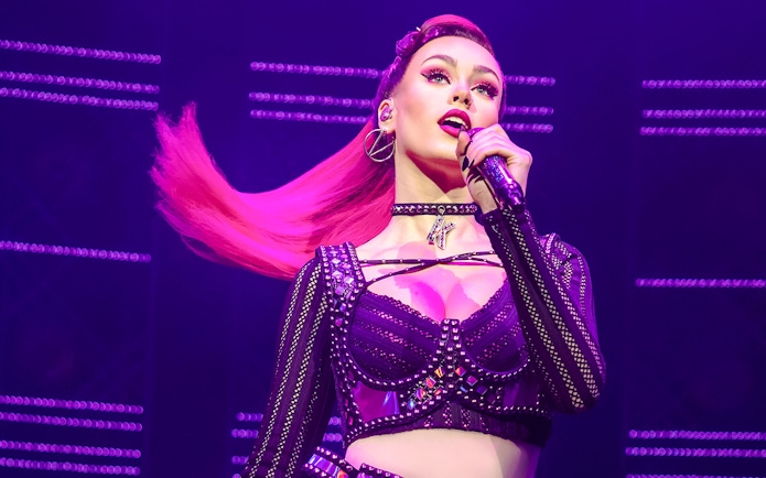 Performer singing on stage during the musical "Six" with vibrant lighting.