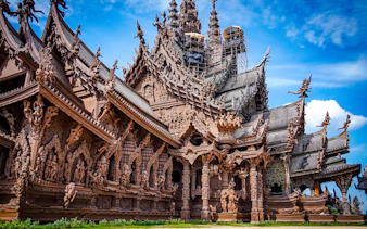 Sanctuary of Truth's intricate wooden carvings under blue sky, Pattaya city tour.