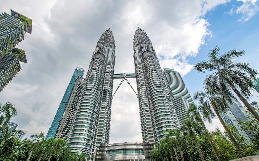 Petronas Twin Towers in Kuala Lumpur with surrounding skyscrapers and palm trees.