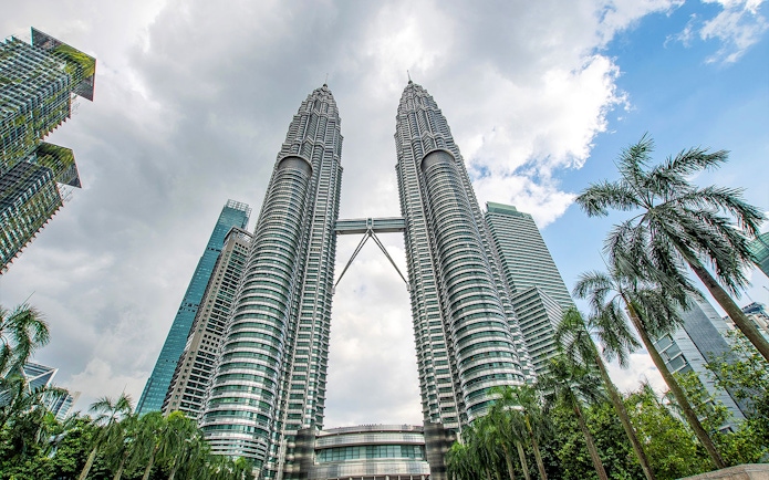 Petronas Twin Towers in Kuala Lumpur with surrounding skyscrapers and palm trees.