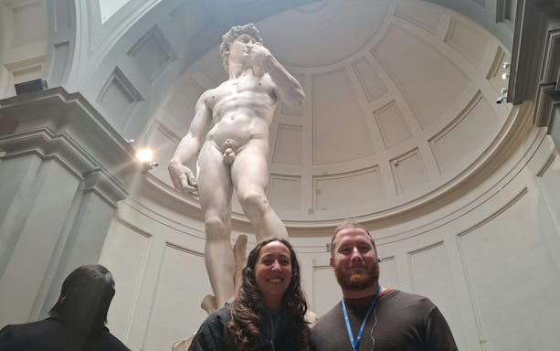 Statue of David in Florence museum with visitors in foreground.