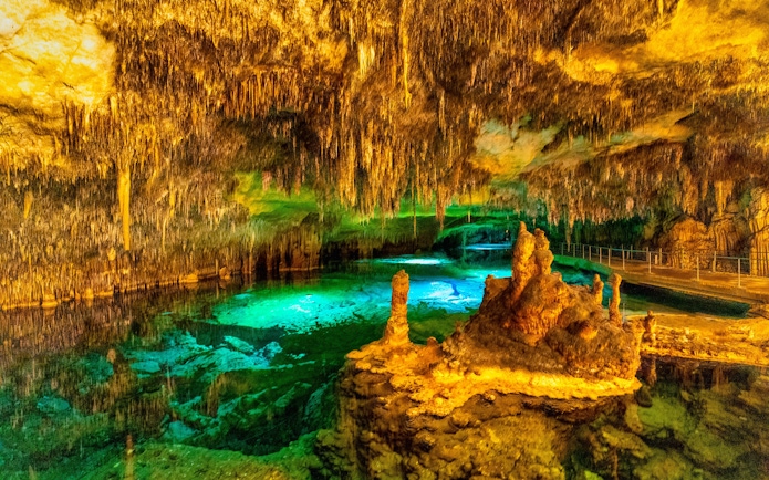Stalactites and stalagmites inside Drach Caves with illuminated underground lake.