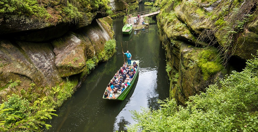 Tourists on a guided boat ride through a narrow gorge near Bastei Bridge, surrounded by lush greenery.