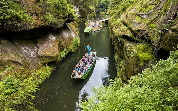 Tourists on a guided boat ride through a narrow gorge near Bastei Bridge, surrounded by lush greenery.