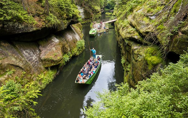 Tourists on a guided boat ride through a narrow gorge near Bastei Bridge, surrounded by lush greenery.