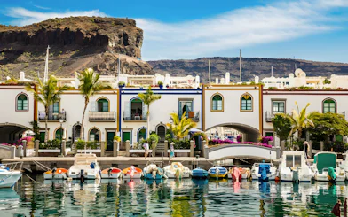 Boats docked along the canal in Puerto de Mogán, Gran Canaria, with colorful buildings and a bridge.