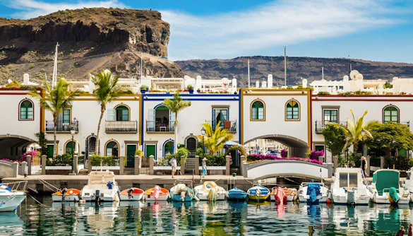 Boats docked along the canal in Puerto de Mogán, Gran Canaria, with colorful buildings and a bridge.