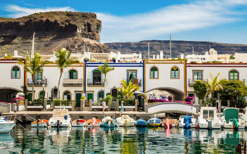 Boats docked along the canal in Puerto de Mogán, Gran Canaria, with colorful buildings and a bridge.