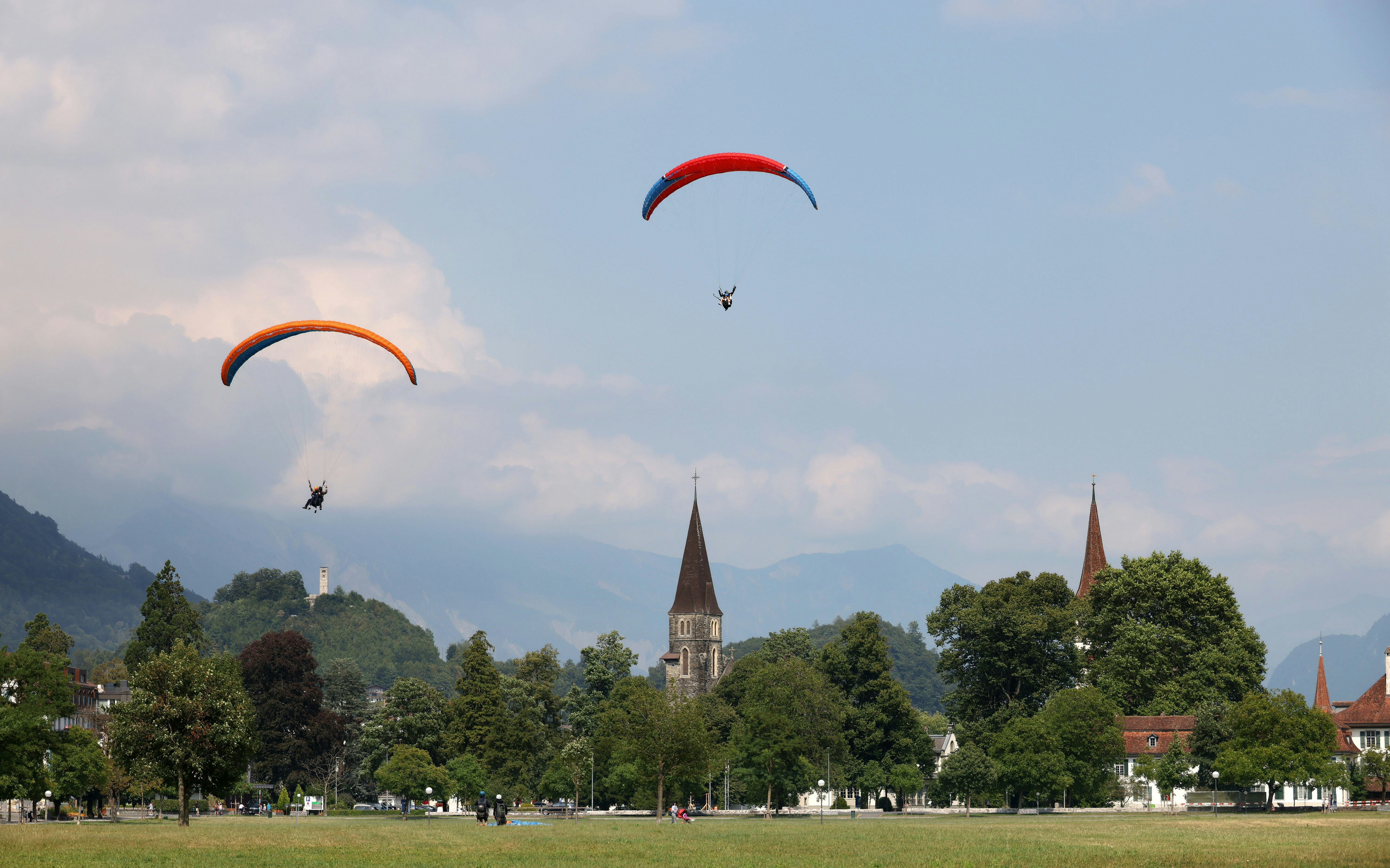 Paragliders soaring over Interlaken with church spires and mountains in the background.